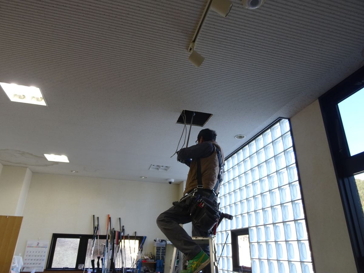 事務所の天井の照明器具を、脚立に乗って施工するスタッフ