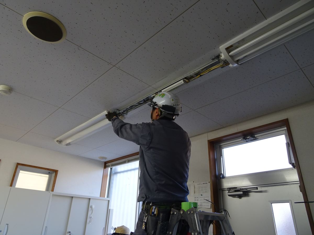 天井の蛍光灯器具を取り付けるスタッフ