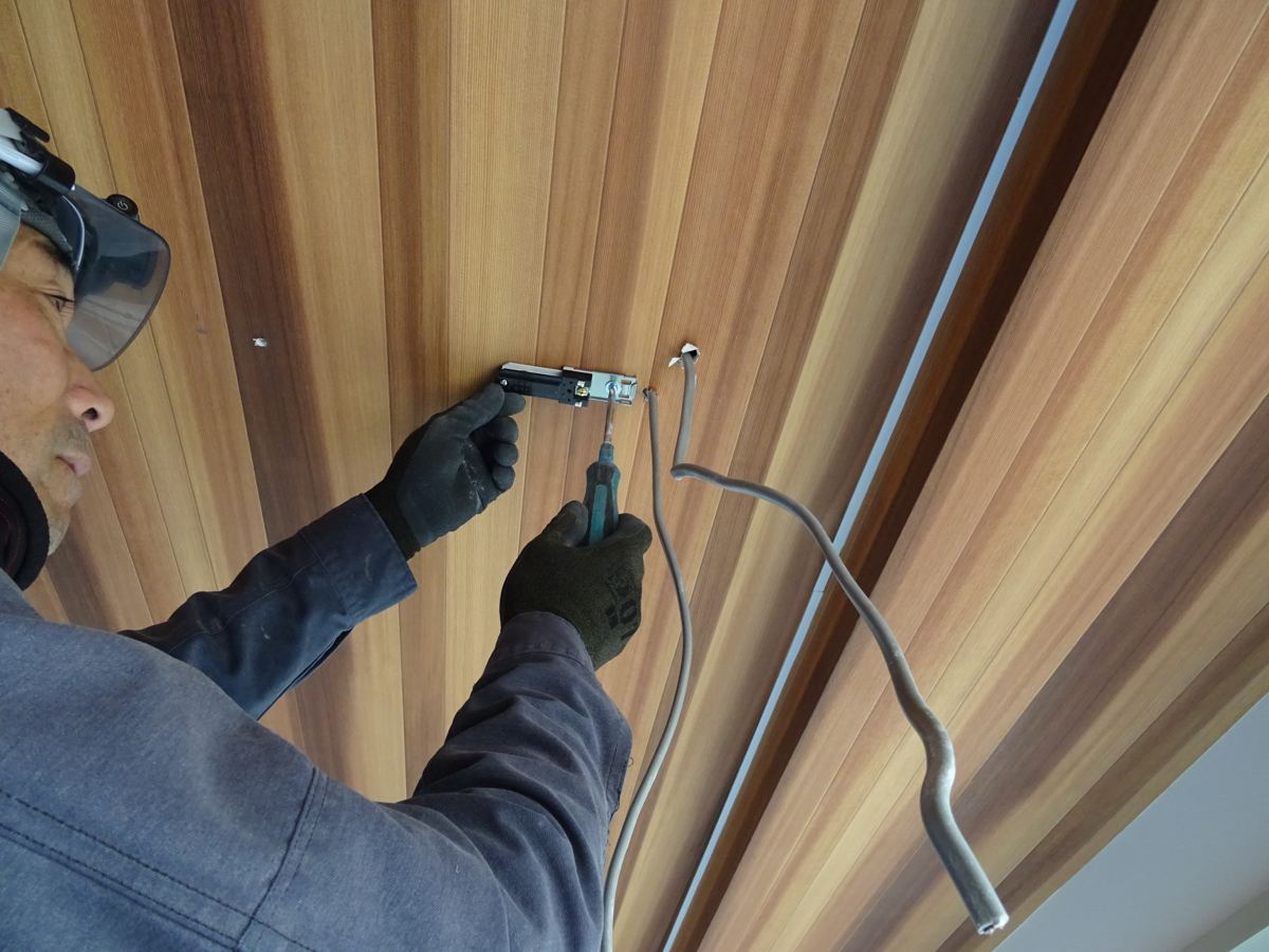 木目の天井で器具を取り付けるスタッフ